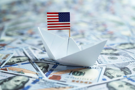 Paper boat with the USA or United States of America flag sailing on dollar banknotes. Concept of economy, financial or governmentの写真素材