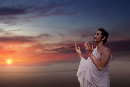 Indonesian southeast asian muslim man wearing white traditional clothes or ihram raises his hand and prays on the hajj. Concept of hajj or umrahの写真素材