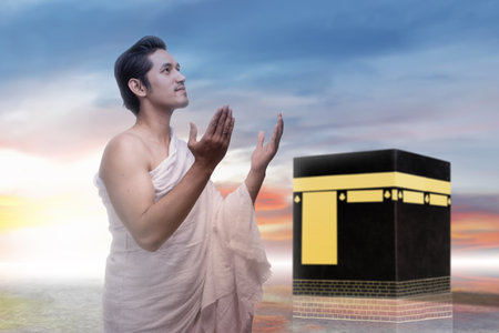 Indonesian southeast asian muslim man wearing white traditional clothes or ihram raises his hand and prays in front of the Kaaba. Concept of hajj or umrahの写真素材