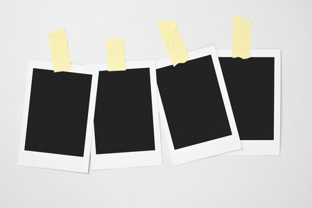 Four blank polaroid photo papers stuck with sticky tape on a white background. Mockup, template, or copy space. Instant camera photo print frameの写真素材