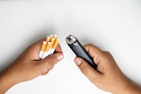 Human hand holding cigarettes, rolled tobacco in paper with a filter tube, and a vape or electronic...