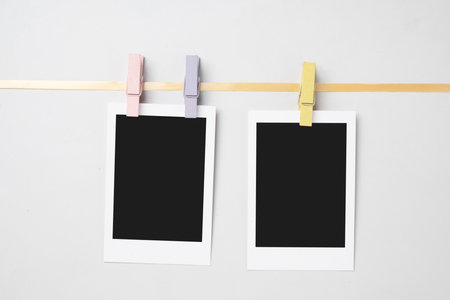 Two blank polaroid photo papers with clothespins hanging on the rope with a white background. Mockup, template, or copy space. Instant camera photo print frameの写真素材