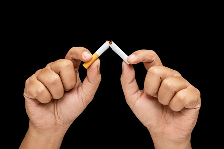 Human hand breaks a cigarette, rolled tobacco in paper with a filter tube, with a black background. Concept of no or quit smoking, a bad habit, and unhealthyの写真素材