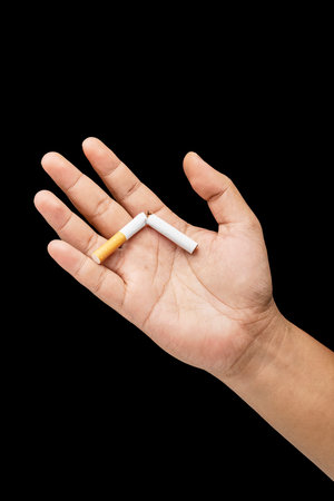 Human hand breaks a cigarette, rolled tobacco in paper with a filter tube, with a black background. Concept of no or quit smoking, a bad habit, and unhealthyの写真素材