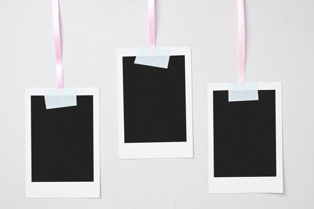 Three blank polaroid photo papers with sticky tape hanging on the rope with a white background. Mockup, template, or copy space. Instant camera photo print frameの写真素材