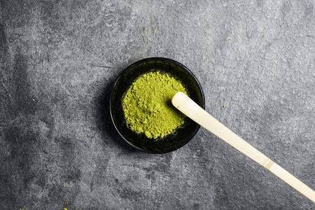 Matcha green tea powder in the black bowl and a traditional bamboo spoon or chashaku on a black table. Accessories for making matcha green tea. Copy space. Top viewの写真素材