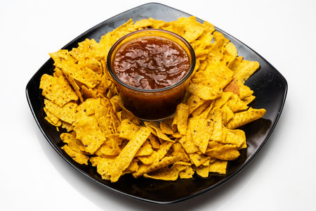 Nachos tortilla chips on the black plate with salsa barbecue sauce in a bowl on a white background. Food and snacks conceptの写真素材