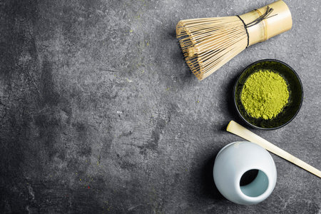 Matcha green tea powder in the black bowl and a traditional bamboo brush whisk with a spoon on a black table. Accessories for making matcha green tea. Copy space. Top viewの写真素材
