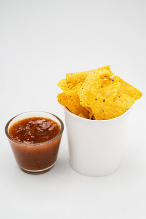 Nachos tortilla chips with salsa barbecue sauce in a glass bowl on a white background. Food and snacks conceptの写真素材