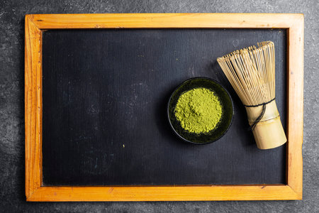 Matcha green tea powder in the black bowl and a traditional bamboo brush whisk or chasen on a black table. Accessories for making matcha green tea. Copy space. Top viewの写真素材
