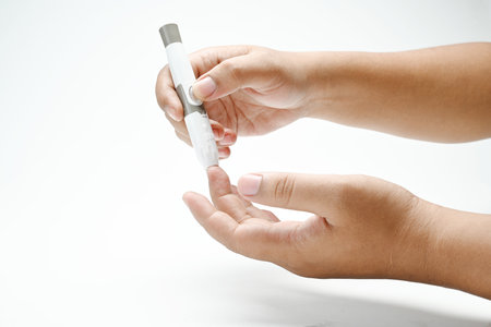 Human hand using a lancet for checking blood sugar level isolated over a white background. Concept of diabetes or a healthy lifestyleの写真素材