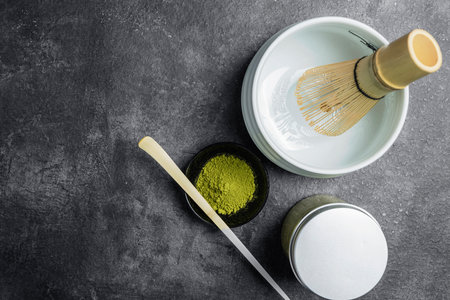 Matcha green tea powder in the black bowl with a wooden spoon and a traditional bamboo brush whisk in an empty bowl on a black table. Accessories for making matcha green tea. Top viewの写真素材