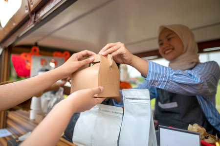 Chinese muslim female in hijab barista serving drinks and snacks to customers. A small business of a...
