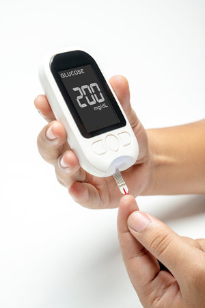 Human hand using a glucometer for checking blood sugar level isolated over a white background. Concept of diabetes or a healthy lifestyleの写真素材