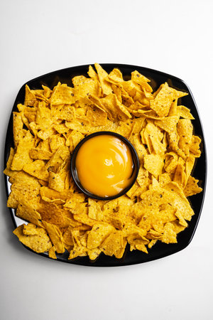 Nachos tortilla chips on the black plate with cheese sauce in a bowl on a white background. Food and snacks conceptの写真素材