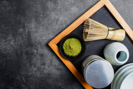 Matcha green tea powder in the black bowl and a traditional bamboo brush whisk or chasen with an empty bowl on a black table. Accessories for making matcha green tea. Copy space. Top viewの写真素材