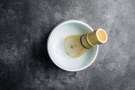 Traditional bamboo brush whisk or chasen in an empty bowl on a black table. Accessories for making matcha green tea. Top viewの写真素材