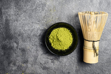 Matcha green tea powder in the black bowl and a traditional bamboo brush whisk or chasen on a black table. Accessories for making matcha green tea. Copy space. Top viewの写真素材