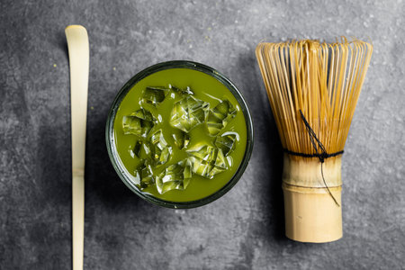 Closeup view of iced matcha green tea on the glass with a traditional bamboo brush whisk or chasen and spoon or chashaku on a black table. Accessories for making matcha green tea. Top viewの写真素材