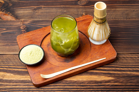 Closeup view of iced matcha green tea on the glass with a traditional bamboo brush whisk or chasen and spoon or chashaku on wooden table. Accessories for making matcha green teaの写真素材
