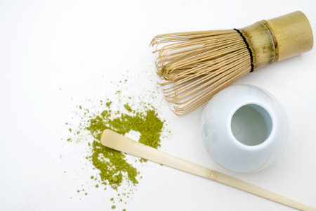 Traditional bamboo brush whisk with a spoon and matcha green tea powder splattered on white...