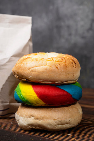 Closeup view of a pile of a collection of bagel breads with various kinds and a brown paper bag on a wooden boardの写真素材