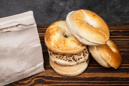 Closeup view of a heap of a collection of bagel breads with various kinds and a brown paper bag on a wooden boardの写真素材