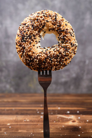Closeup view of the fork with a bagel bread with sesame seeds standing on a wooden tableの写真素材