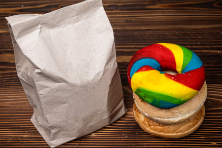 Closeup view of a pile of a collection of bagel breads with various kinds and a brown paper bag on a wooden boardの写真素材