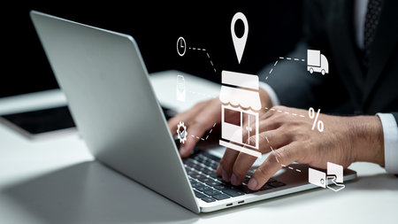 Businessman using a laptop while showing an icon of a shop for ecommerce. Tablet on the table. Technology innovation on a virtual screen. Concept of ecommerce or small businessの写真素材