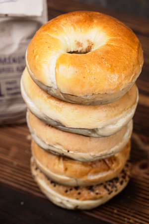 Closeup view of a pile of a collection of bagel breads with various kinds and a brown paper bag on a wooden boardの写真素材