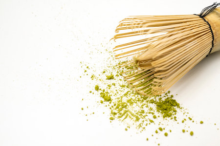 Matcha green tea powder with a traditional bamboo brush whisk or chasen on a white background....