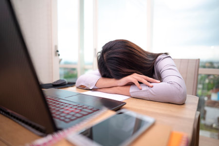 Indonesian southeast asian businesswoman experiencing stress and burnout while working on laptop in hybrid workplace. Paperwork and a cellphone on the table. Business concept. Remote working from homeの写真素材