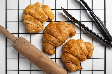 Tongs and rolling pin with freshly baked croissants on a cooling tray with a white background. Top viewの写真素材