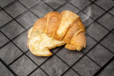 Slice of freshly baked croissant on a cooling tray with a black background