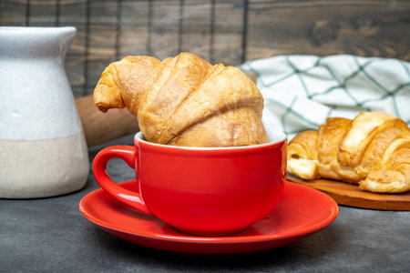 Freshly baked croissant in a cup of coffee with a rolling pin and a napkin on the tableの写真素材