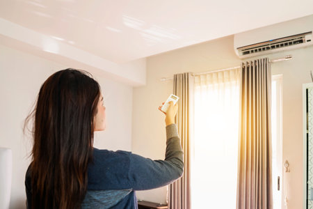 Indonesian southeast asian woman turns off the air conditioner in the bedroom in the morning. Self-care and wellness routines conceptの写真素材