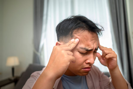 Indonesian southeast asian man in the living room with mental health, fatigue, and sad problems. Faced with depression, frustration, tiredness, headaches, and stress. Healthcare conceptの写真素材