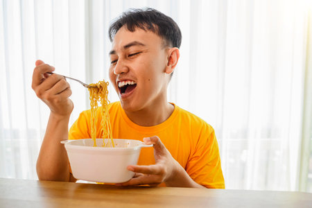 Indonesian southeast asian man sitting at a table and eating tasty instant noodles at home