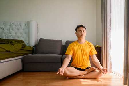 Indonesian southeast asian man meditating in the lotus position on yoga at home for a healthy lifestyle and body care. Meditation and yoga practices conceptの写真素材