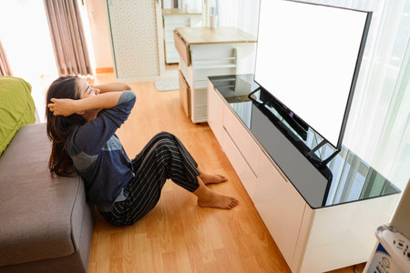 Indonesian southeast asian woman watching television with depression and worry for distress and angry. Mental health and mindfulness concept. Empty television screen for mockup, template or copy spaceの写真素材