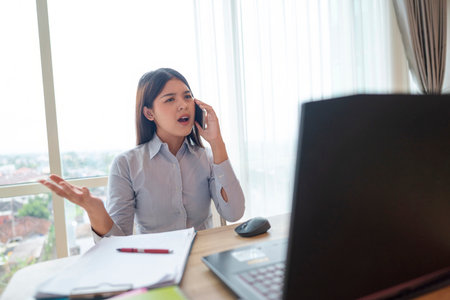 Indonesian southeast asian businesswoman working with paperwork while talking on the cellphone with...