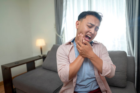 Indonesian southeast asian man touching her mouth with his hand with a painful expression because of a toothache or dental illness on his teeth. Healthcare conceptの写真素材