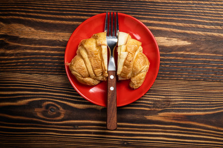 Slices of freshly baked croissants with a fork on a red plate with a wooden background. Top viewの写真素材