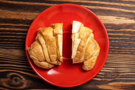 Slices of freshly baked croissants on a red plate with a wooden background. Top viewの写真素材