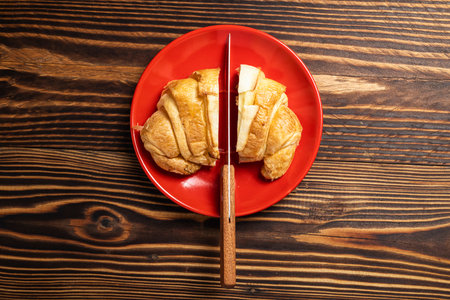 Slices of freshly baked croissants with a knife on a red plate with a wooden background. Top viewの写真素材