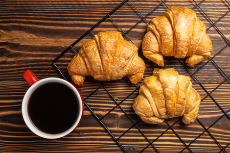 Freshly baked croissants on a cooling tray and a cup of coffee with a wooden background. Top viewの写真素材