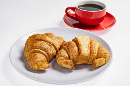 Freshly baked croissants on a plate with a cup of coffee on a white backgroundの写真素材