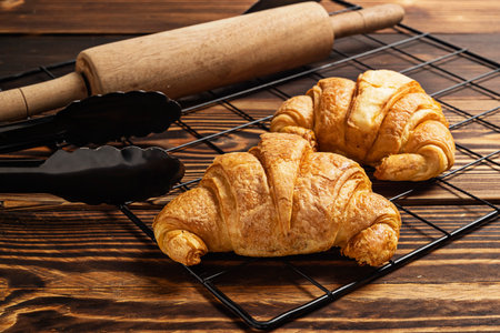 Freshly baked croissants on a cooling tray with tongs and a rolling pin on the tableの写真素材