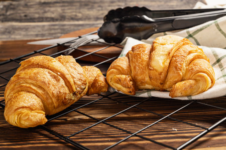 Freshly baked croissants on a cooling tray with tongs and a napkin on the tableの写真素材